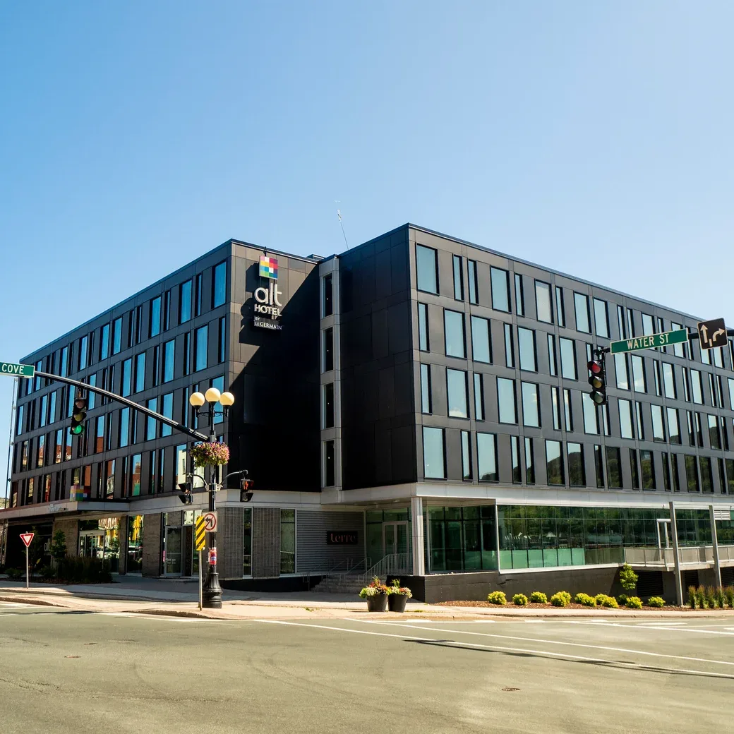 Representative hotel space: A modern hotel building stands on a city street corner beneath a clear sky.