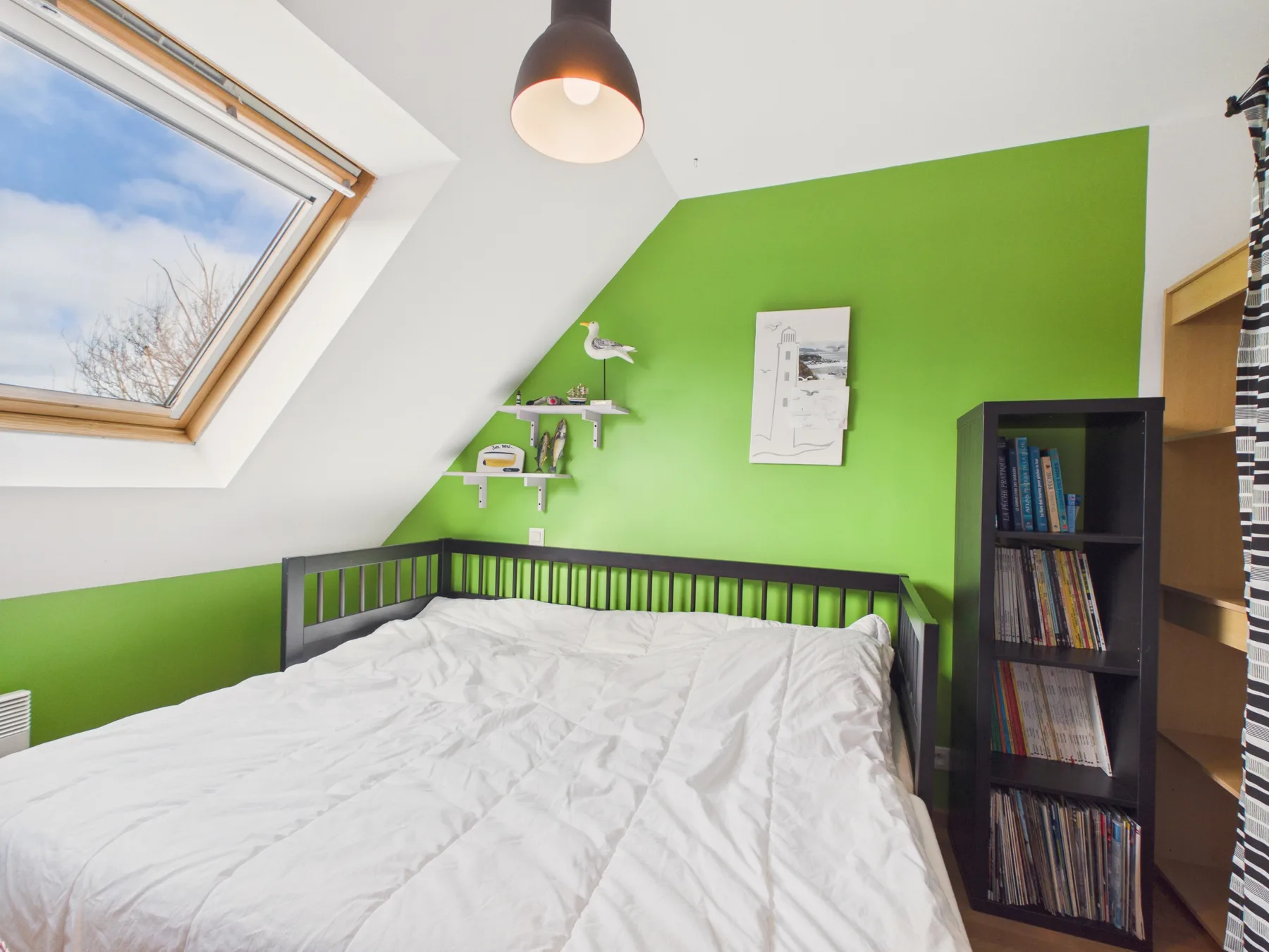A bedroom with a bed beneath a sloped ceiling and a bright green wall.