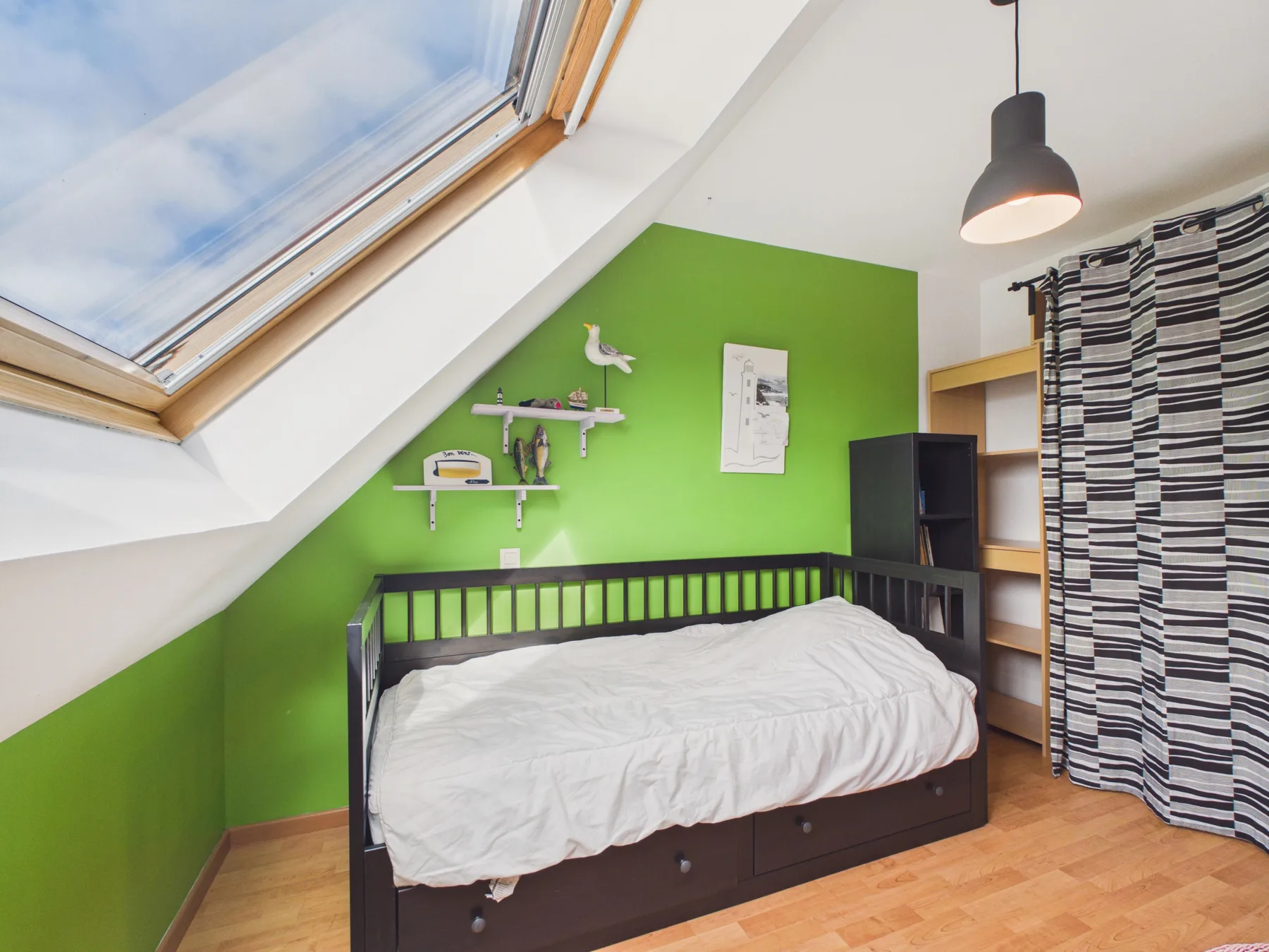 A bedroom with a bed against a bright green wall beneath a sloped skylight.