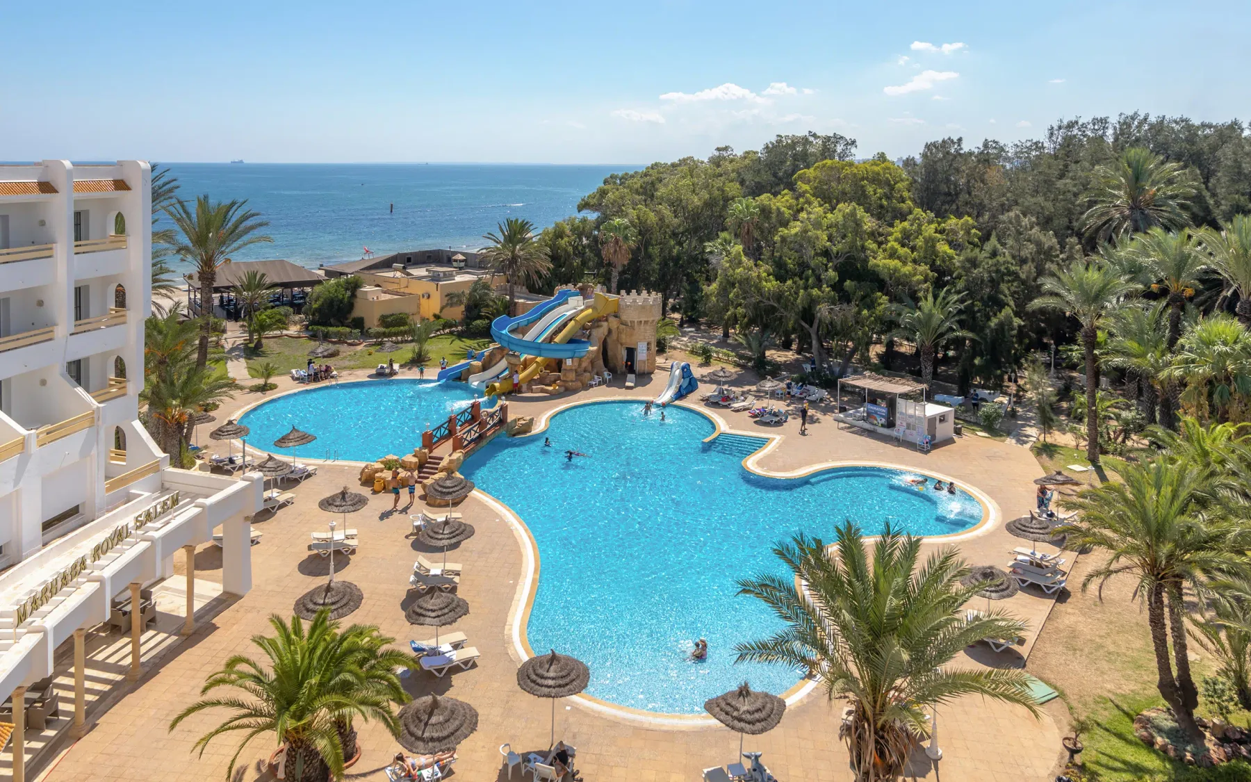 Espacio representativo del hotel: Una gran piscina al aire libre con asientos, palmeras y el mar al fondo.