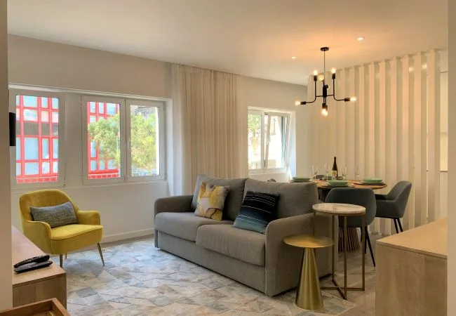 A living and dining area with gray seating, a dining table, and large windows.