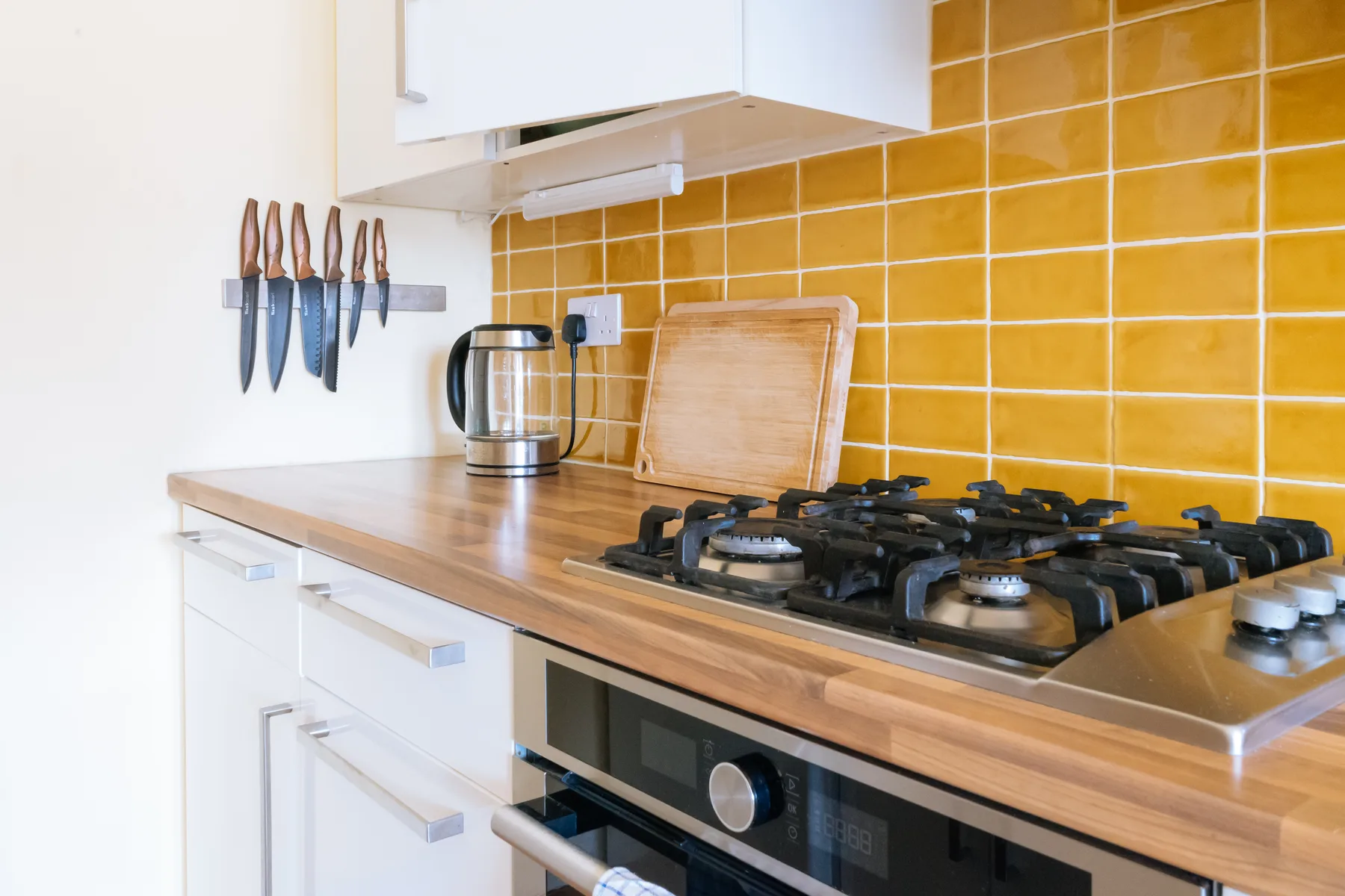 Una encimera de cocina con estufa de gas, hervidor y azulejos naranjas.
