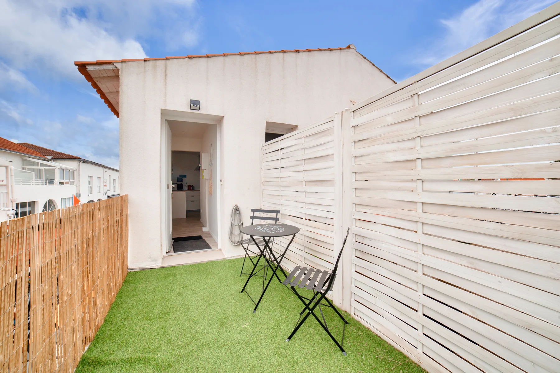 A small outdoor patio with artificial grass, a table, and seating beside a white building.