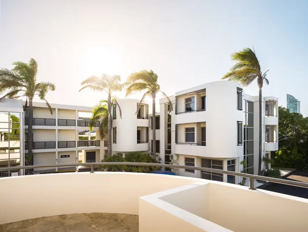 Representative hotel space: A curved balcony overlooks a white multi-story building and several palm trees.