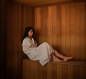 Representative hotel space: A woman in a robe sits on a bench inside a wood-paneled sauna.