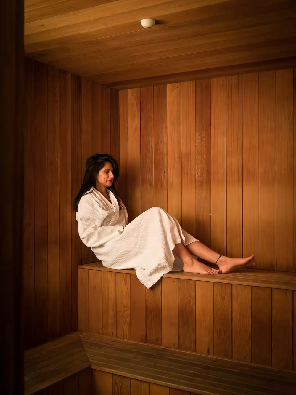Representative hotel space: A woman in a robe sits on a wooden bench in a wood-paneled sauna.