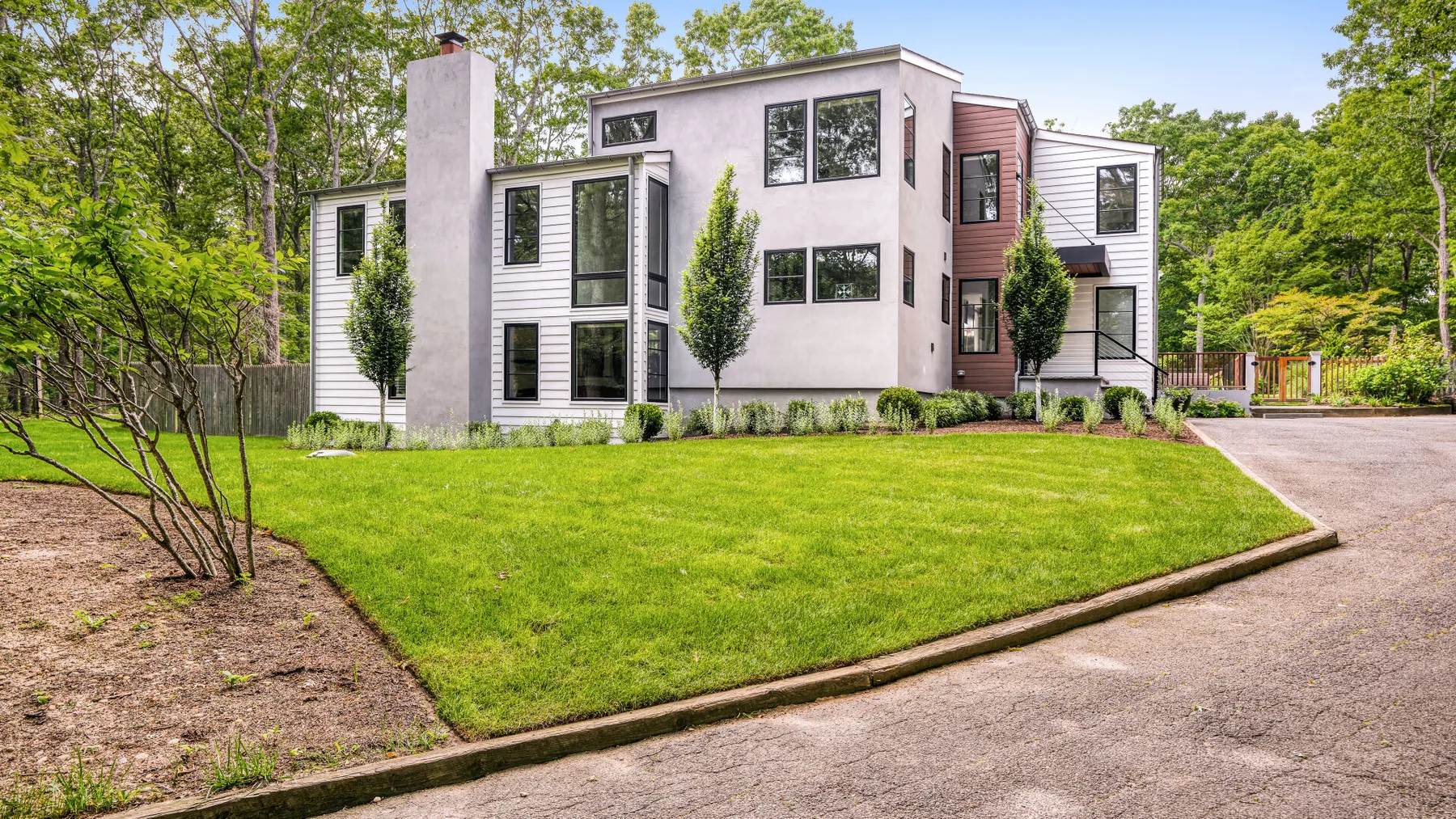 A modern house stands beside a broad green lawn and paved driveway.