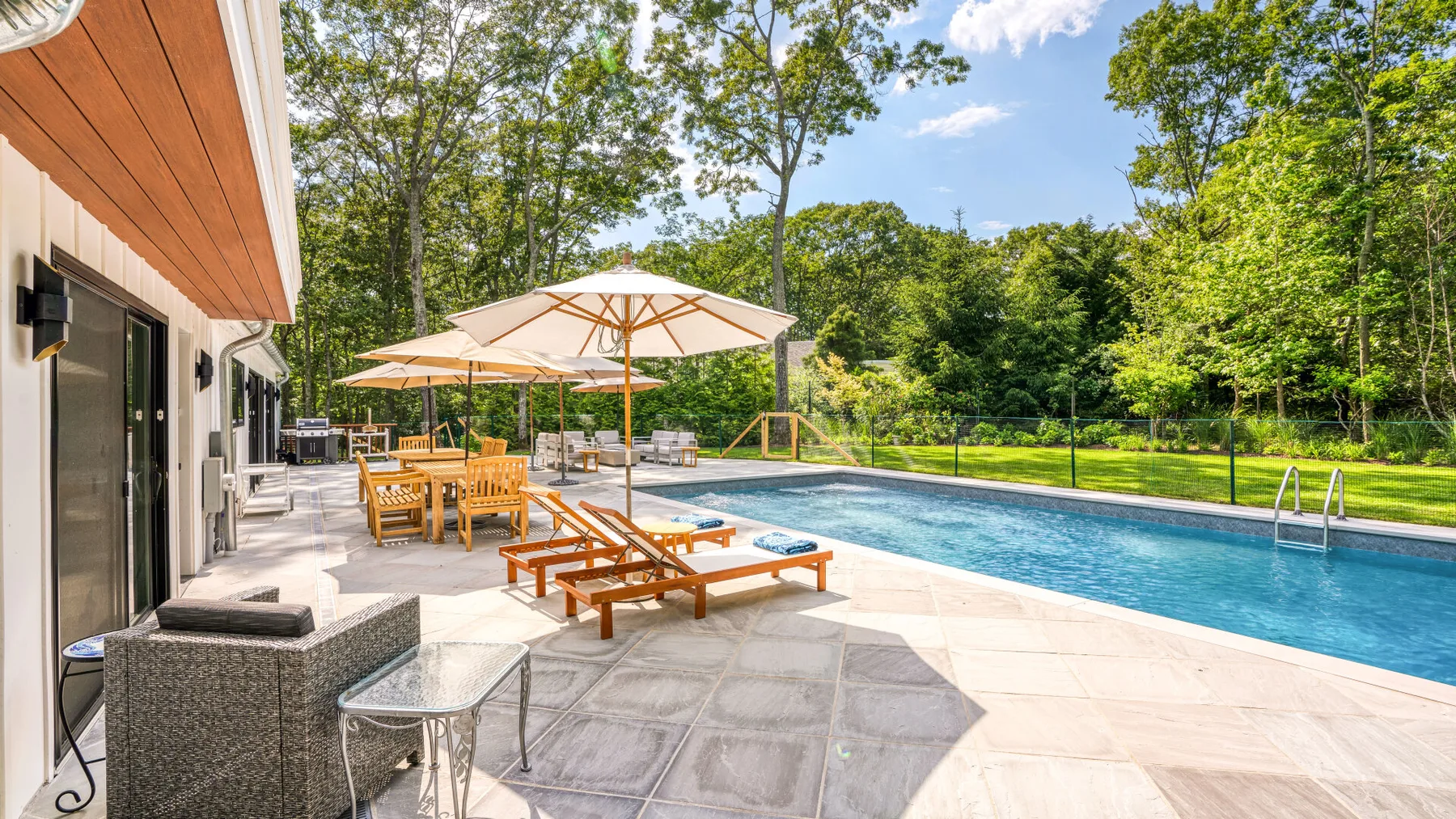 A backyard patio with lounge seating and umbrellas beside a swimming pool.