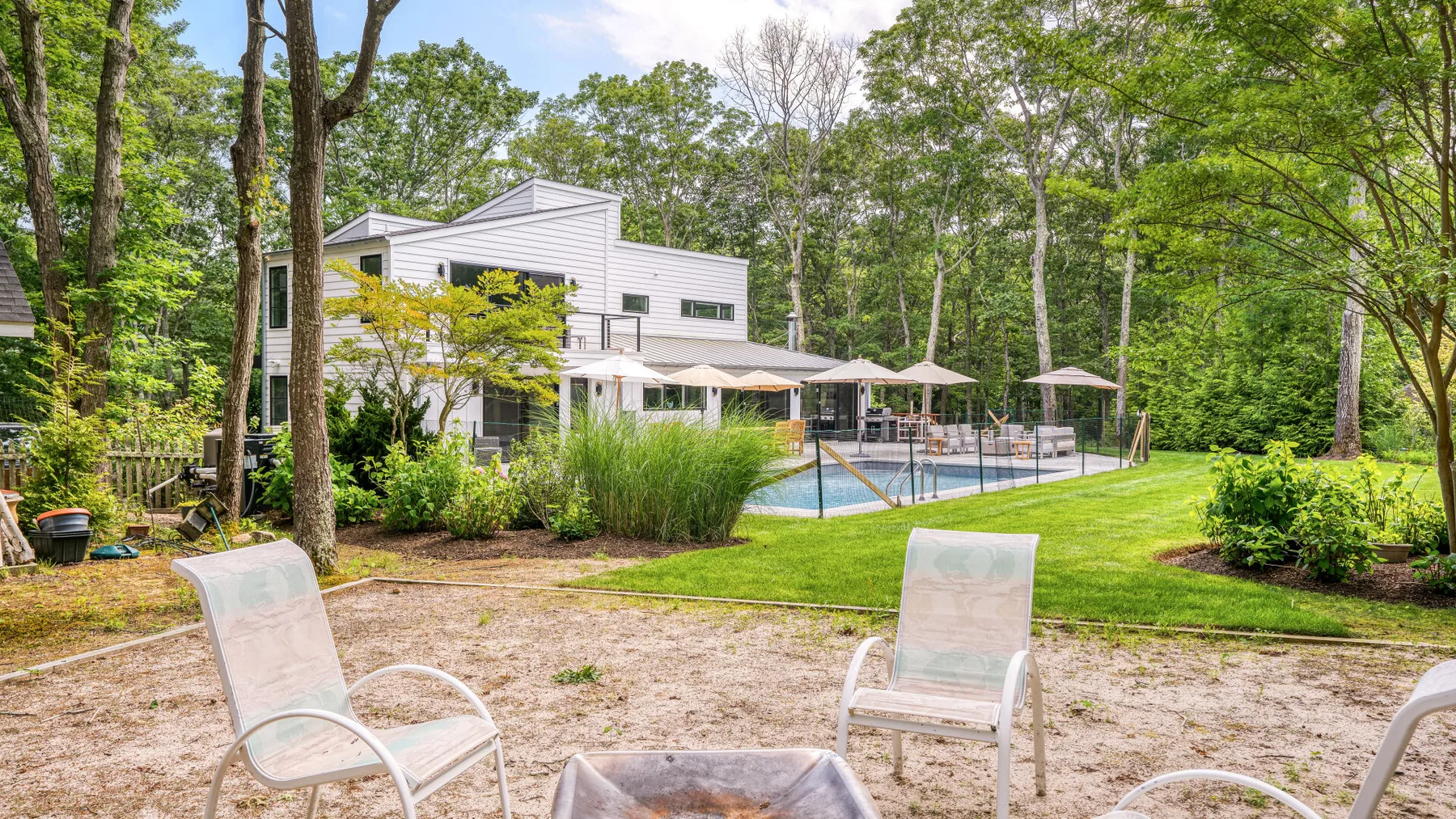 A wooded outdoor pool area with patio seating beside a modern building.