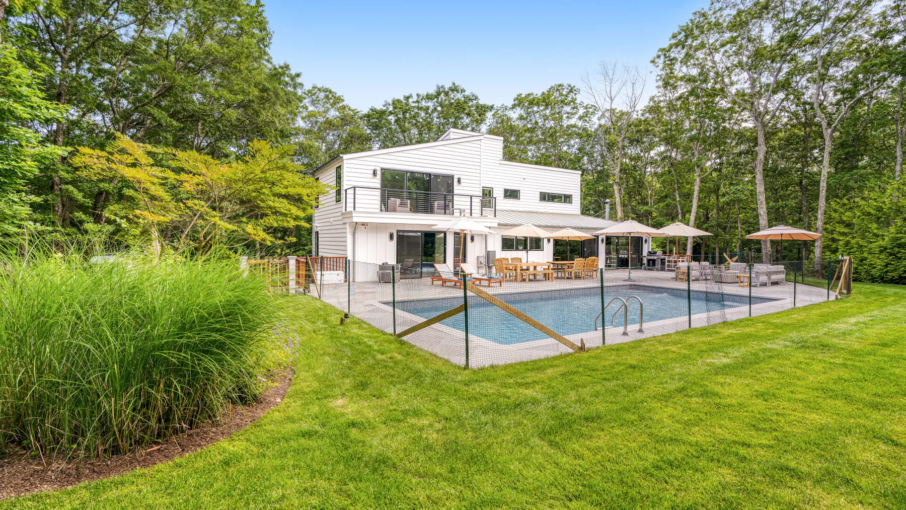 A modern house overlooks an outdoor swimming pool surrounded by lawn and trees.