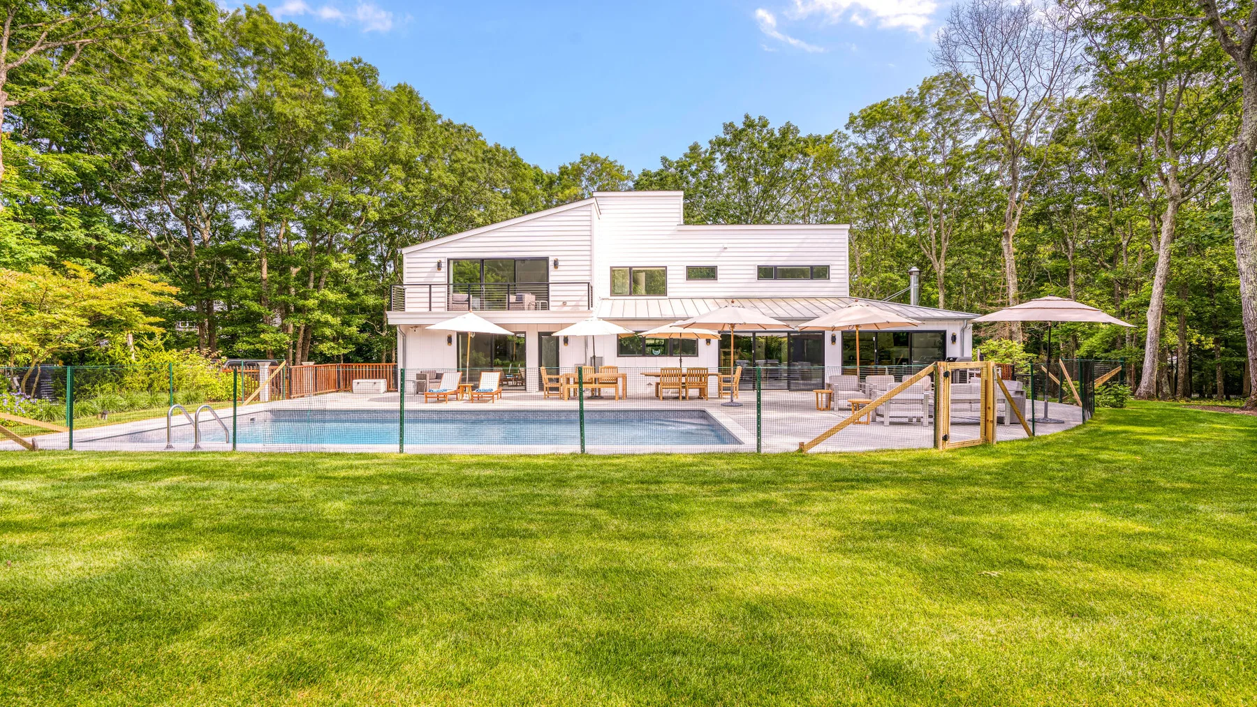 A modern house with a swimming pool and lawn in a wooded setting.
