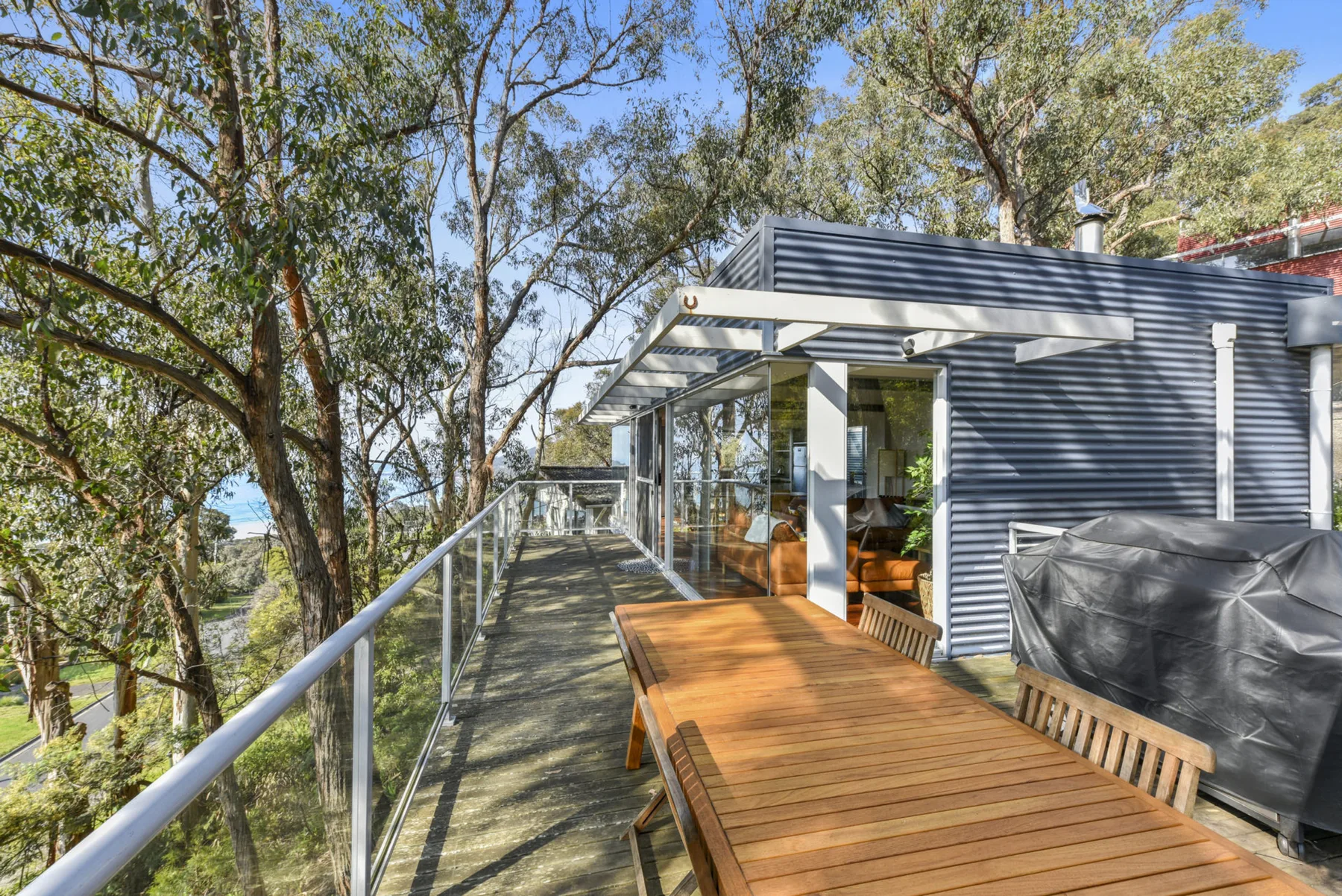 An outdoor deck beside a modern building, with a long wooden table and trees nearby.