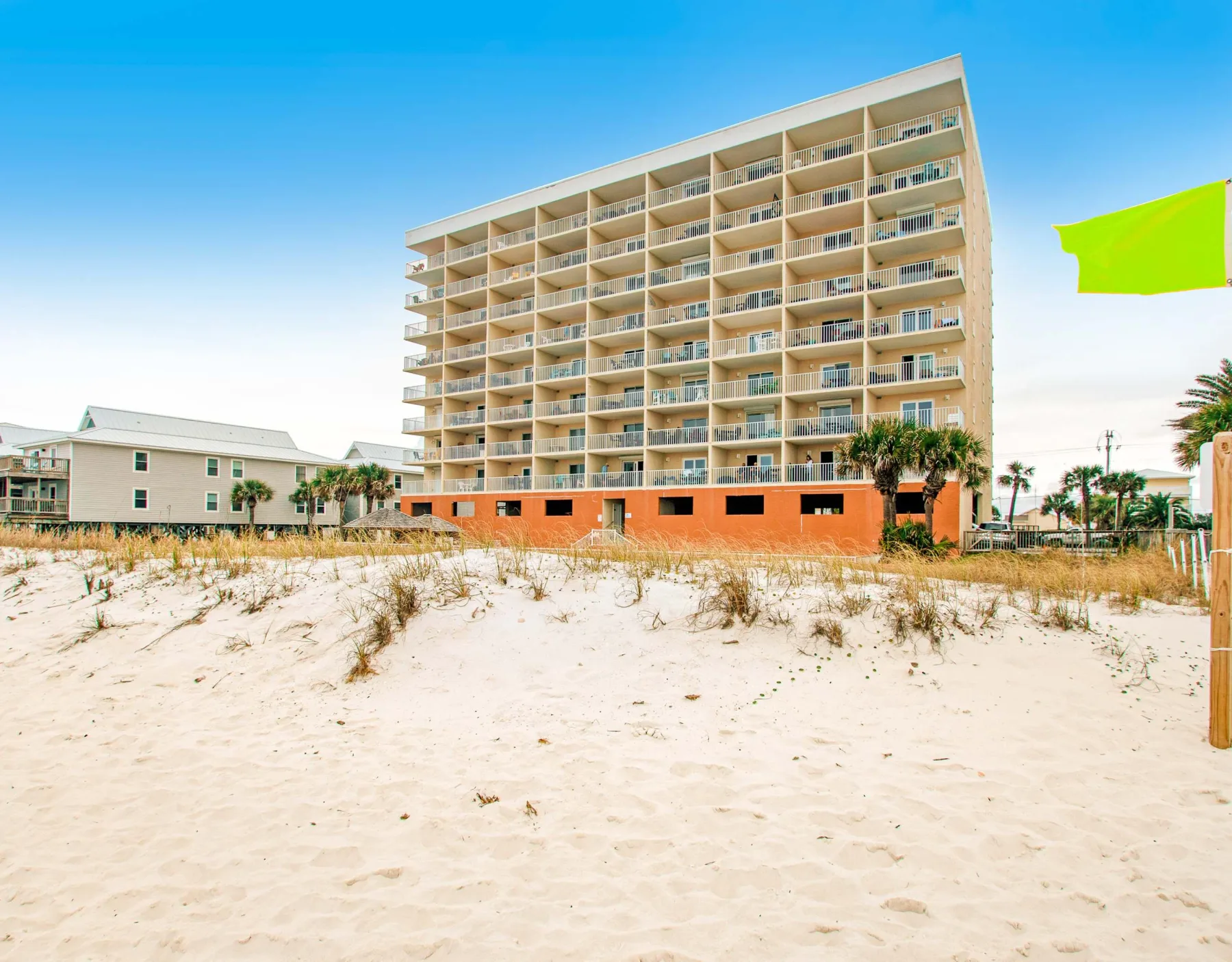 Zona común: Un edificio de apartamentos junto a la playa se alza detrás de una duna de arena.