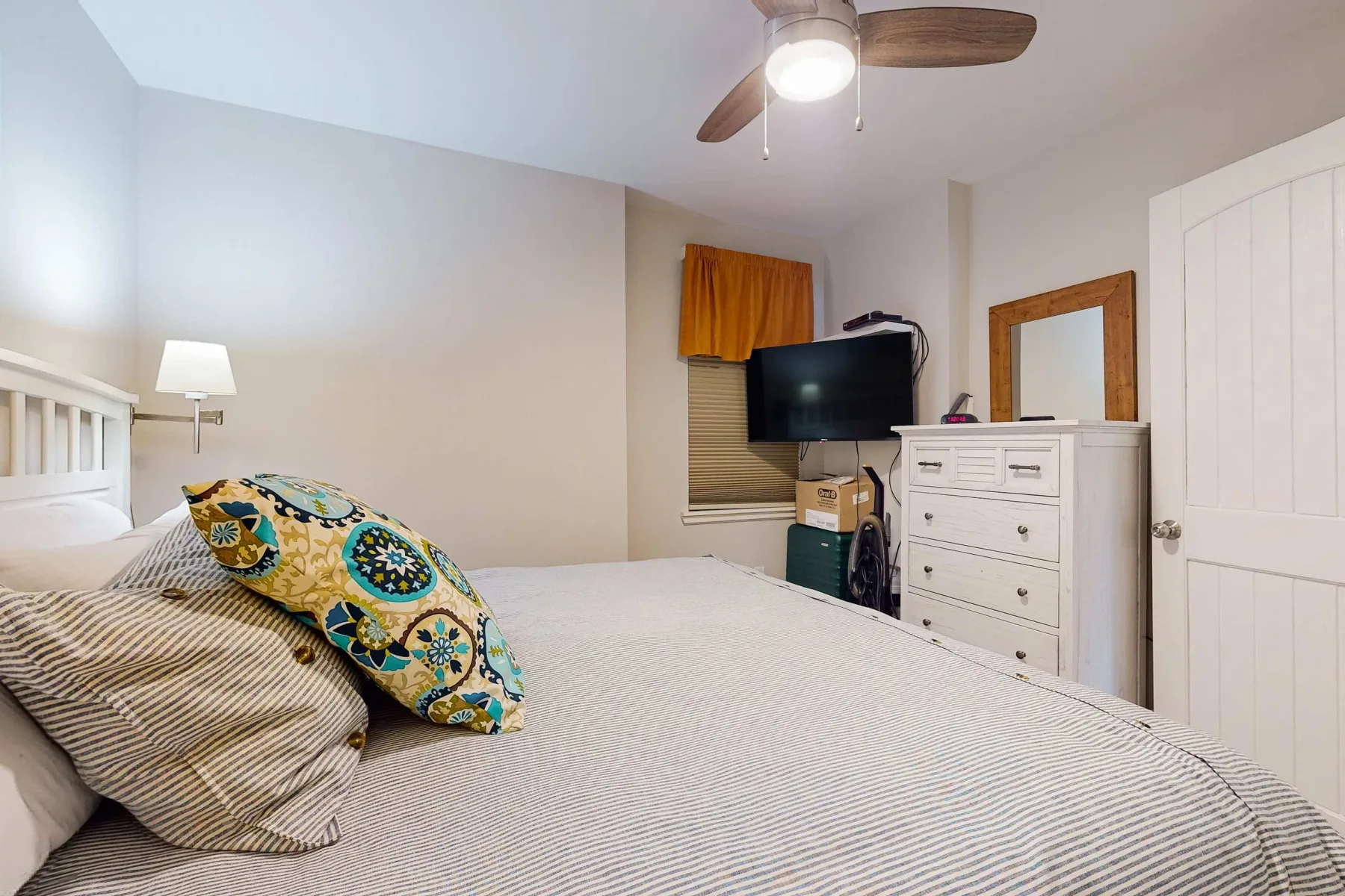 Un dormitorio con una cama, una cómoda y un televisor junto a la ventana.