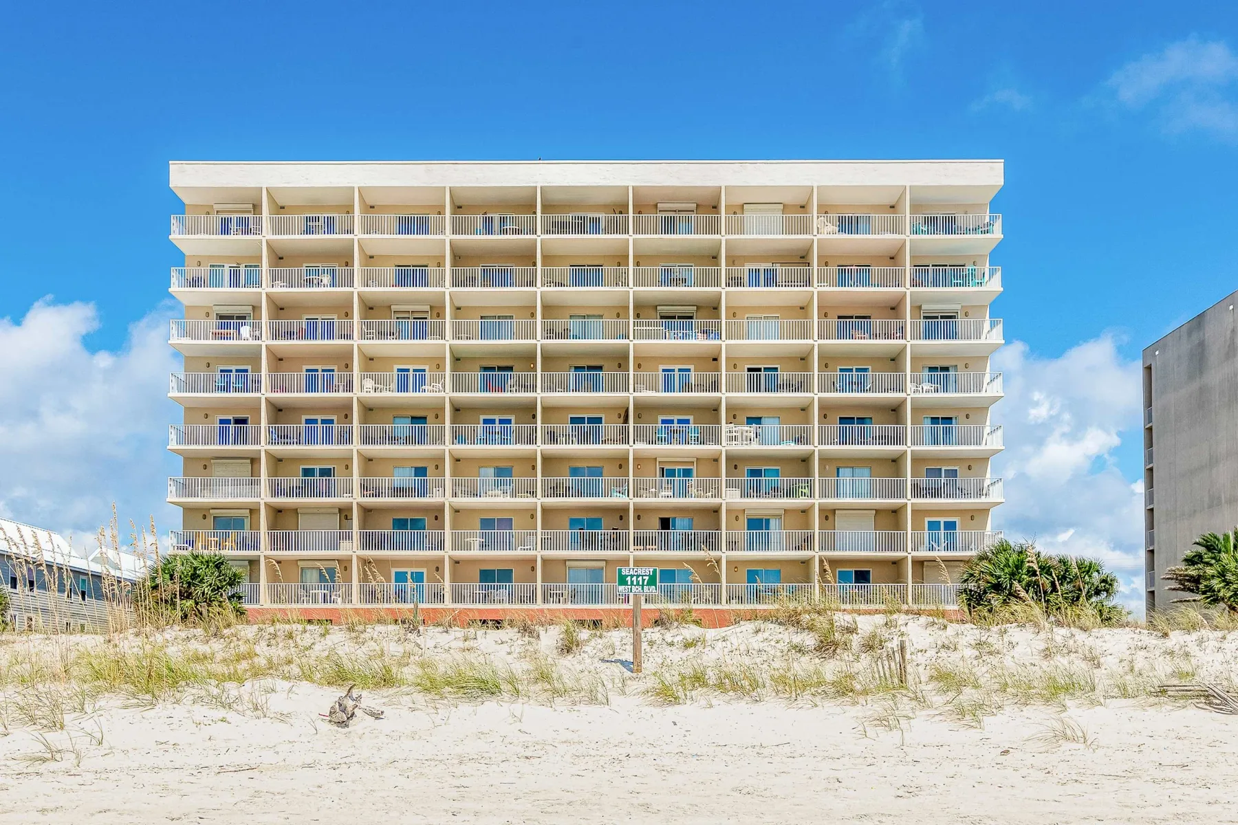 Zona común: Un edificio de apartamentos junto a la playa se alza detrás de una duna de arena.