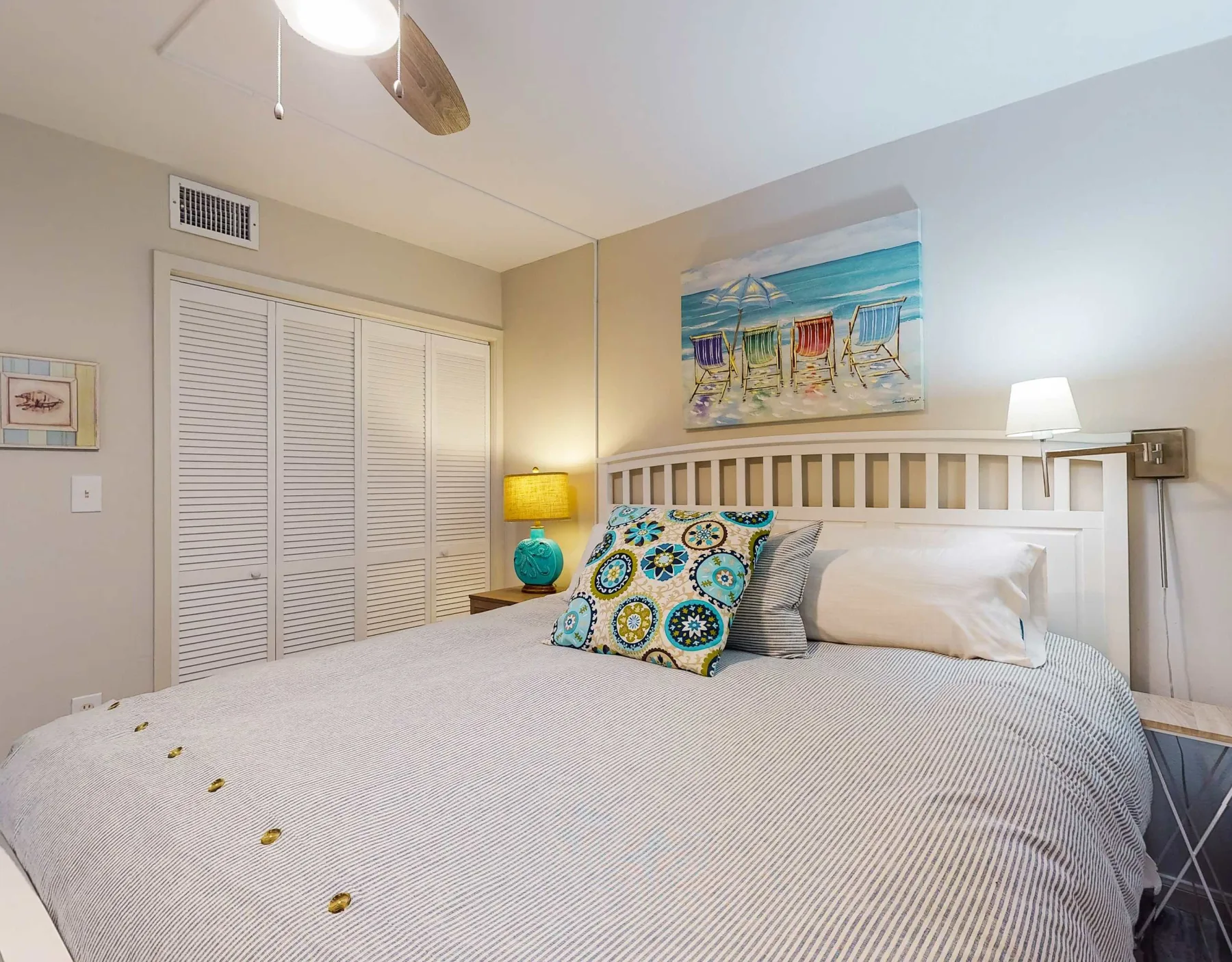 Un dormitorio con una cama grande, almohadas coloridas y arte playero en la pared.