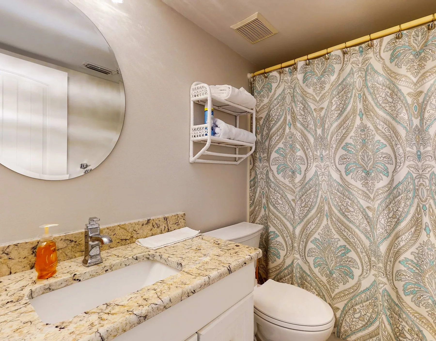 Baño con lavabo, inodoro y cortina de ducha estampada.