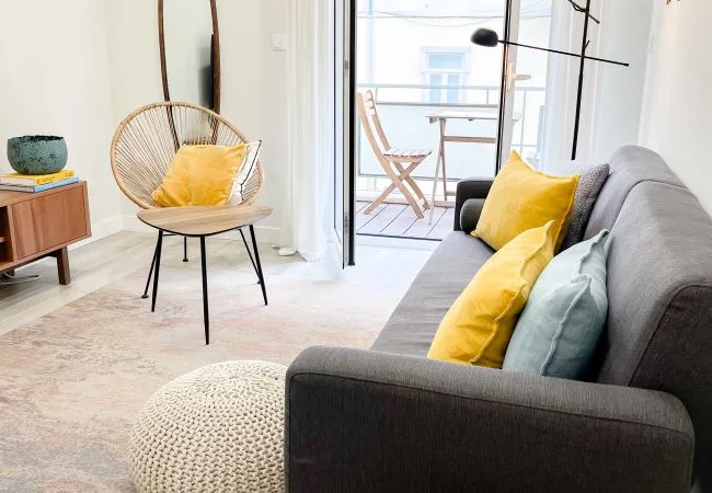 A bright living room with seating beside an open glass door to a balcony.