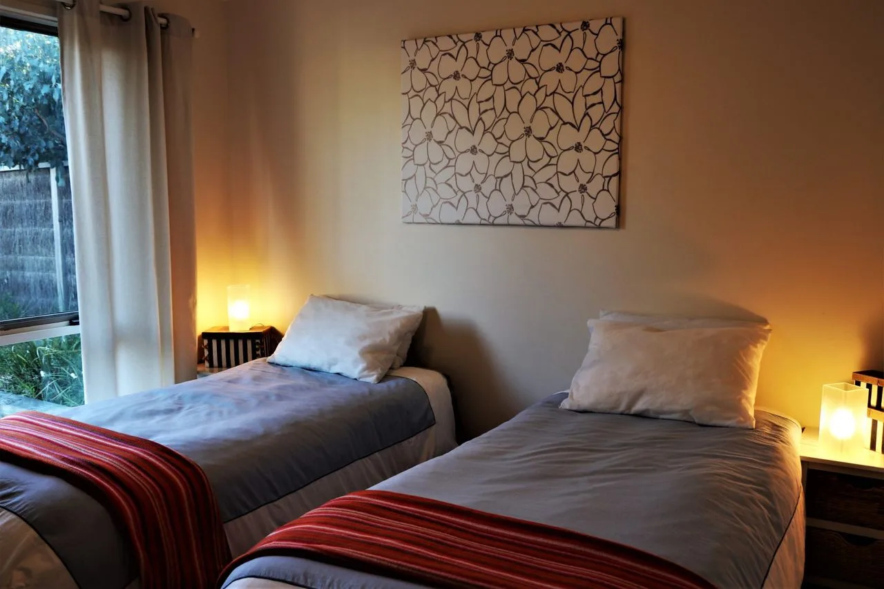 Un dormitorio con dos camas, ropa de cama neutra y arte en la pared.