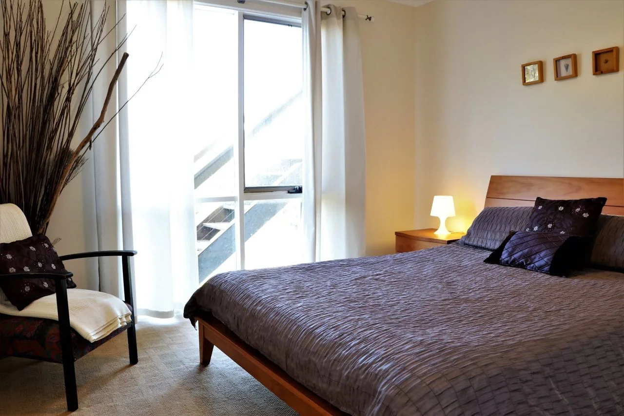 Un dormitorio con una cama grande, una lámpara de noche y una puerta corrediza de vidrio.