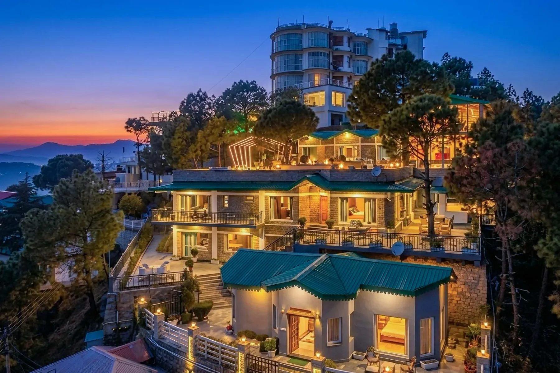 Un conjunto de edificios en una ladera brilla con luces cálidas al atardecer.