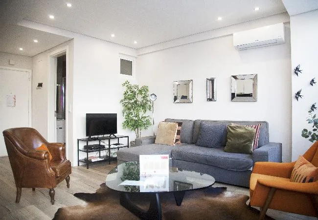 A bright living room with a gray sofa, glass coffee table, and television.