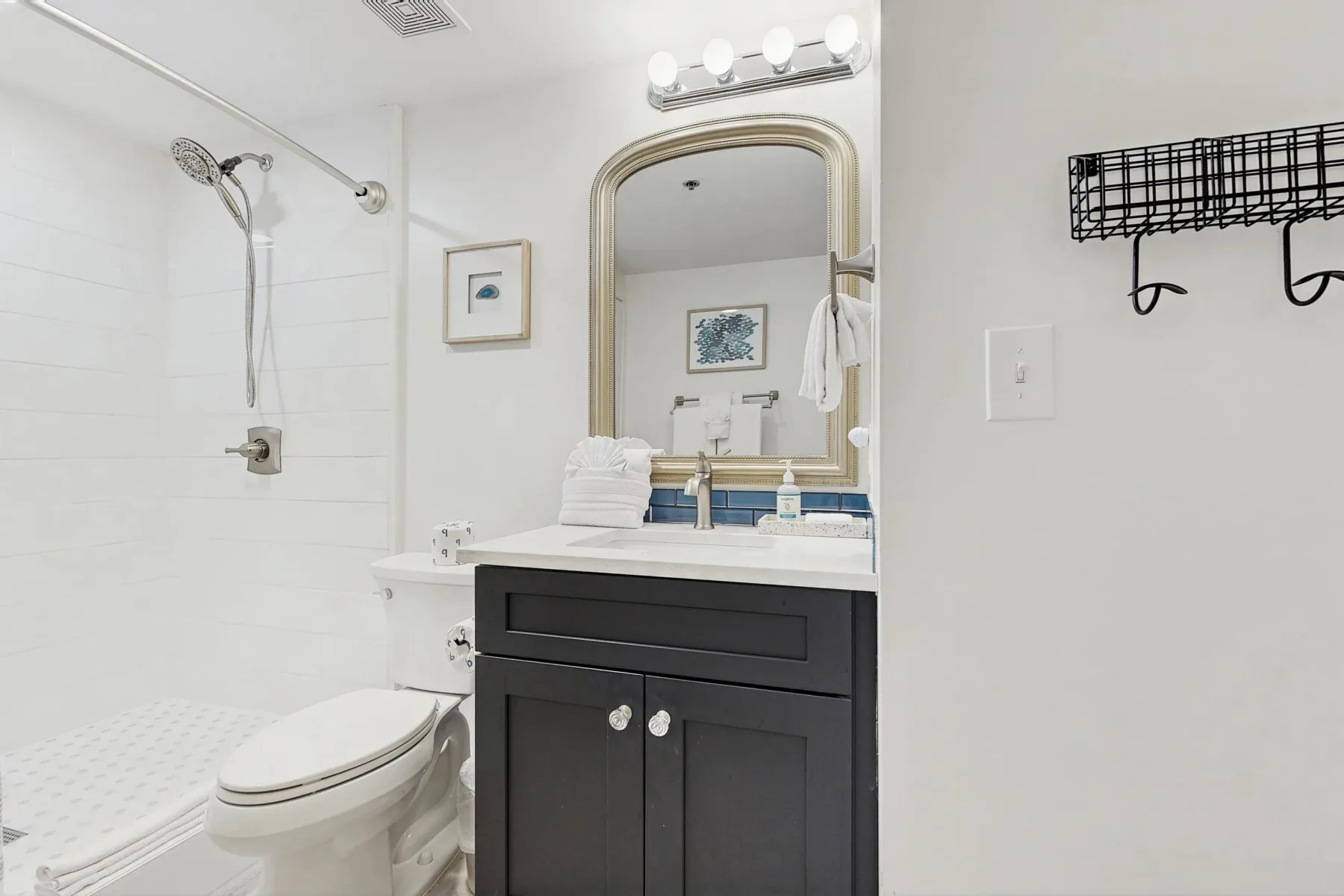 Un baño con ducha, inodoro y tocador oscuro bajo un espejo grande.