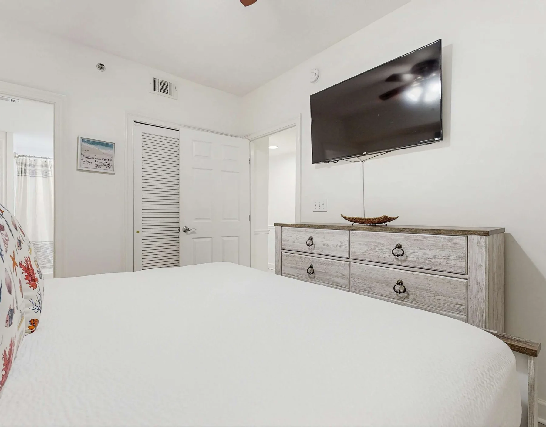 Un dormitorio con una cama en primer plano y un televisor montado sobre una cómoda.