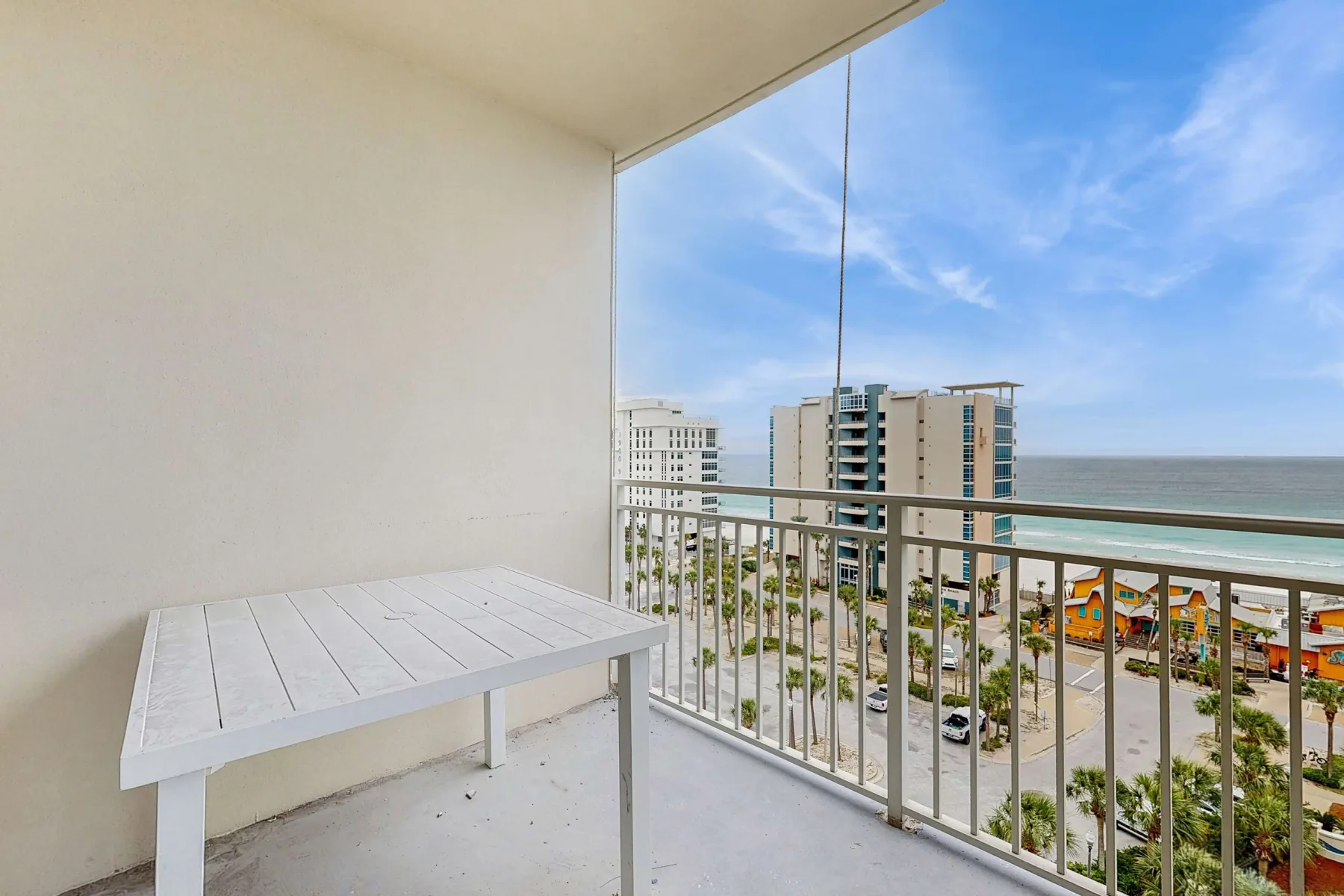 Un balcón con una mesa blanca da a edificios cercanos y al océano.