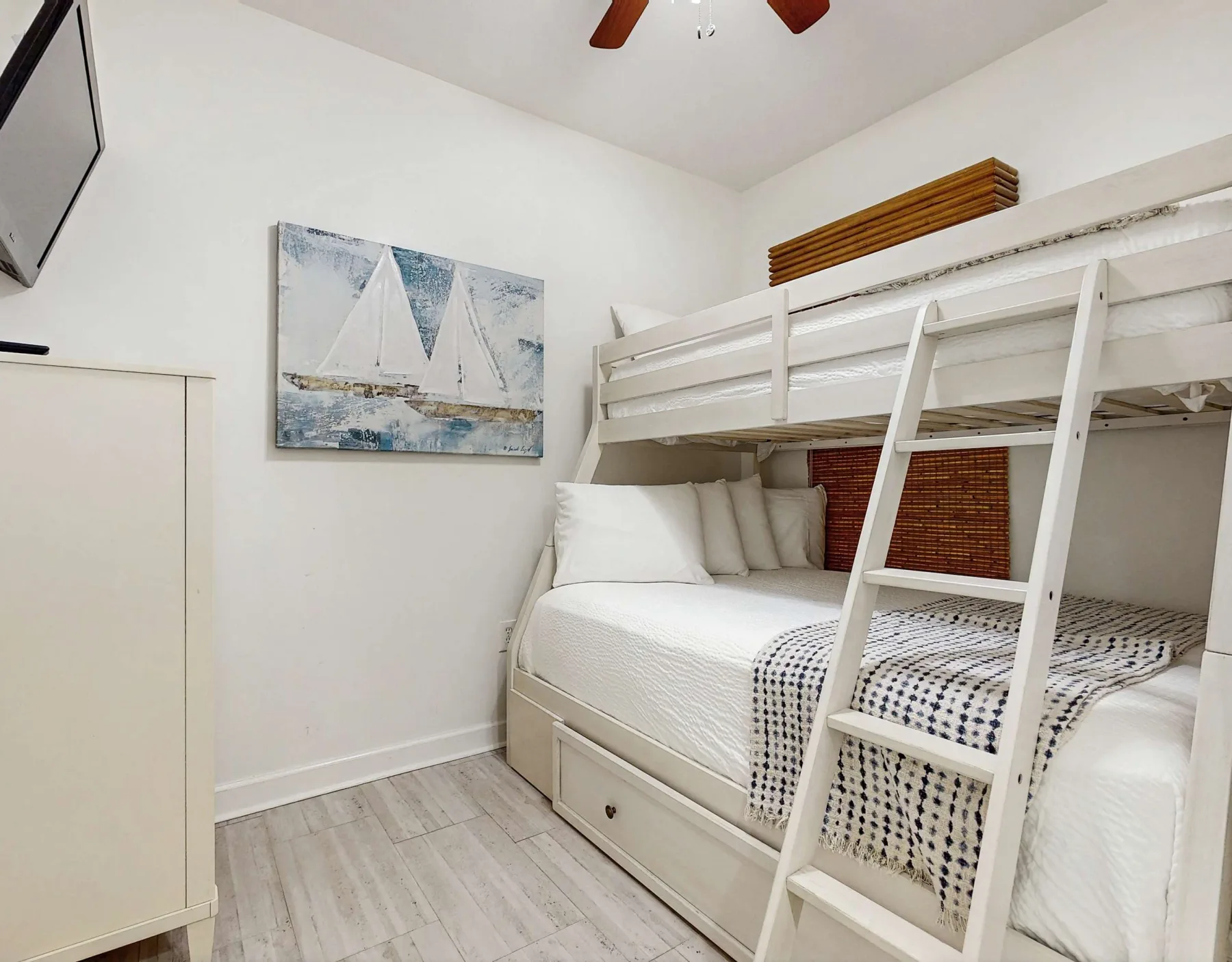 Un dormitorio con literas, ropa de cama blanca y un cuadro de veleros.