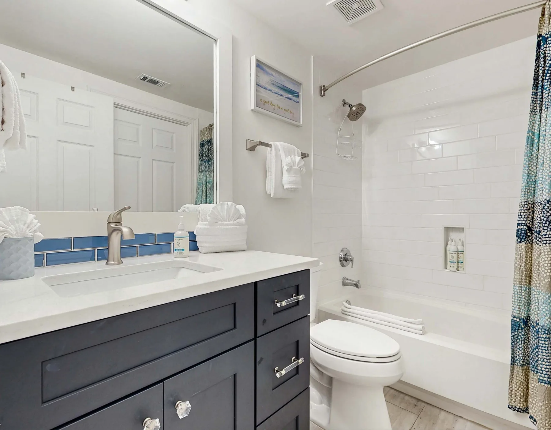 Un baño luminoso con tocador oscuro, lavabo blanco, inodoro y bañera.
