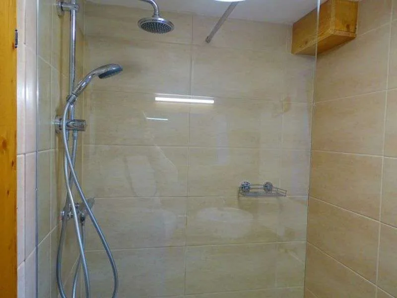 Una zona de ducha con azulejos, un cabezal fijo y una ducha de mano.