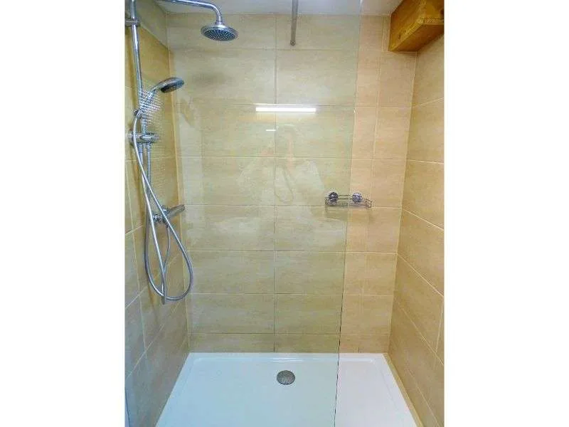 Una zona de ducha con azulejos, ducha de mano y base blanca.