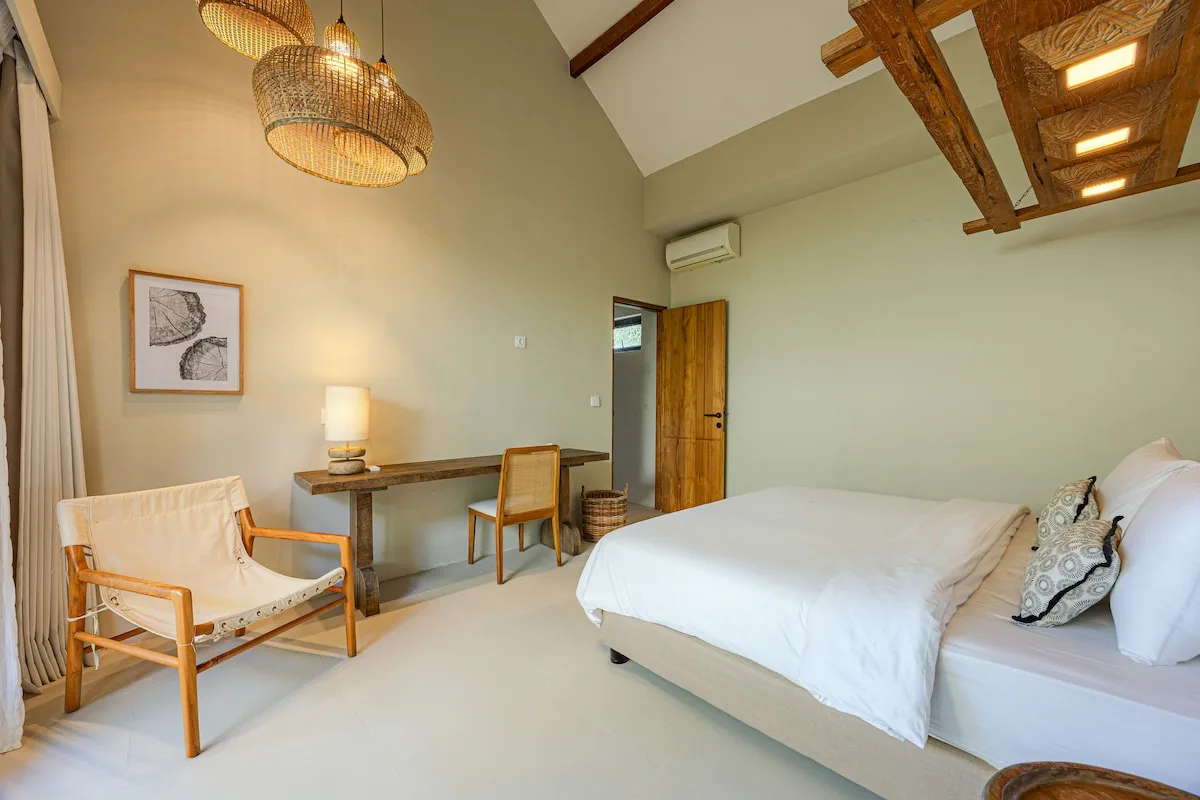 A bedroom with a neatly made bed, desk, and woven pendant lights.