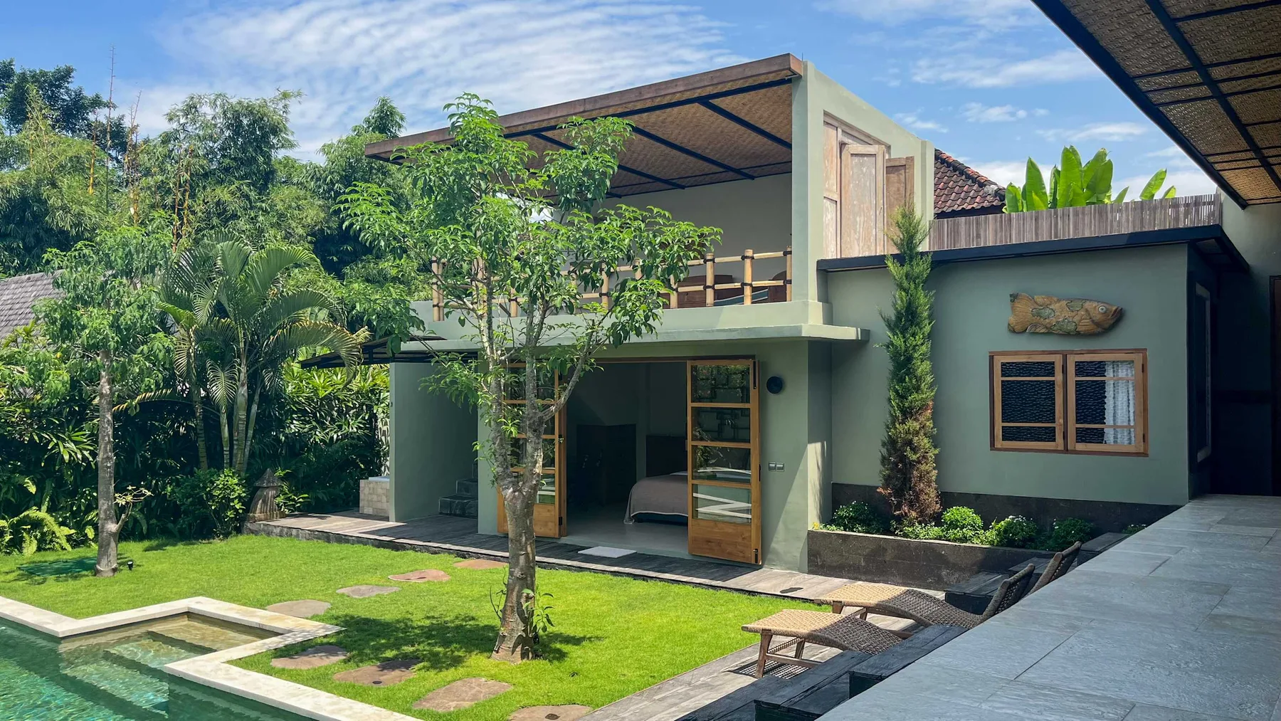 A modern house opens onto a green lawn and outdoor seating area.
