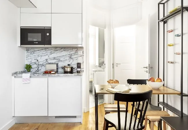 Una luminosa cocina con comedor y una mesa junto a gabinetes blancos.