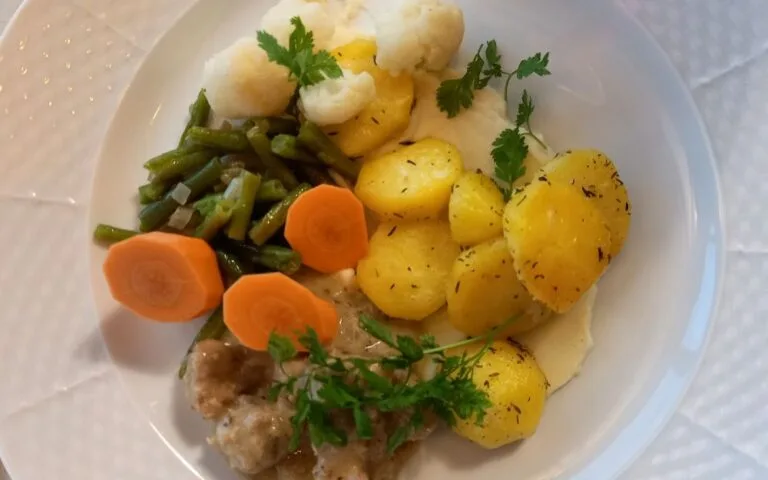 Espacio representativo del hotel: Un plato de verduras cocidas y papas adornado con hierbas frescas.