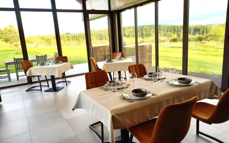 Espacio representativo del hotel: Comedor con mesas preparadas junto a grandes ventanales con vistas a campos verdes.
