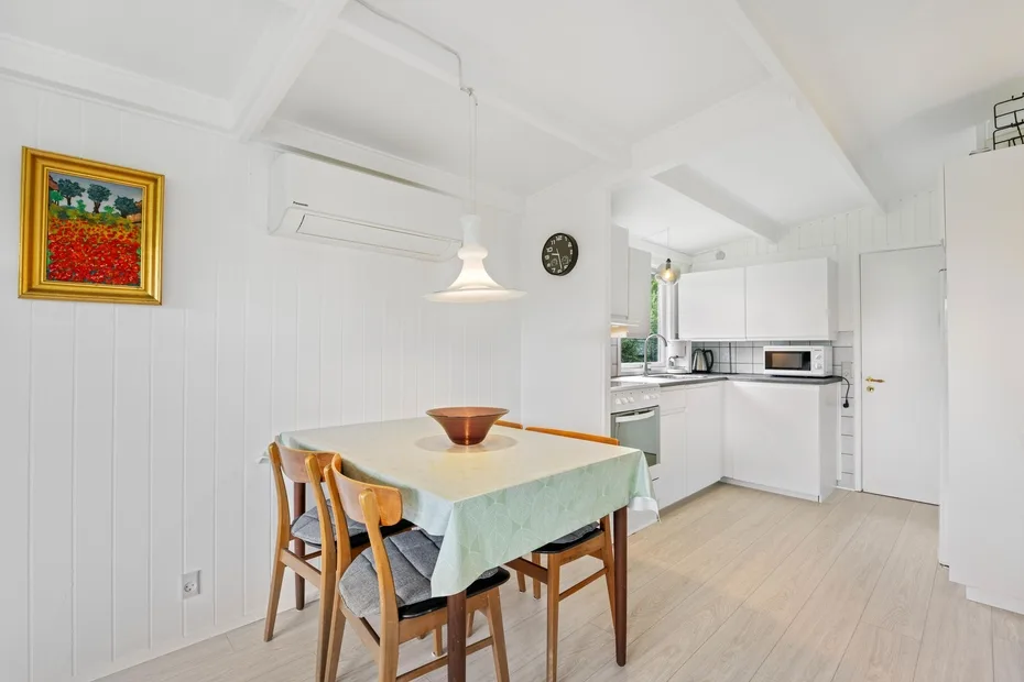 A bright dining area with a table and a compact kitchen in the background.