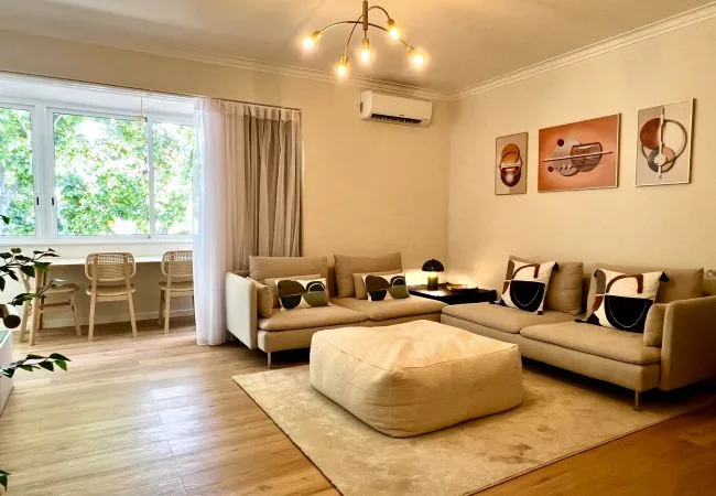 A bright living room with an L-shaped seating area and a large ottoman.