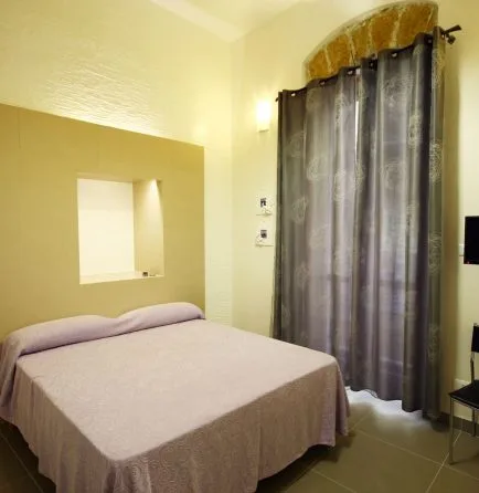 Representative hotel space: A bedroom with a double bed and dark curtains beside a tall arched window.