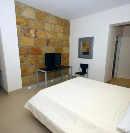 Representative hotel space: A bedroom with a bed, television, and exposed stone wall.