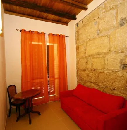 Representative hotel space: A seating area with a red couch beside orange curtains and an exposed stone wall.