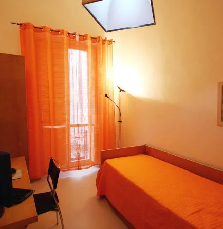Representative hotel space: A bedroom with a bed beside a window with orange curtains.