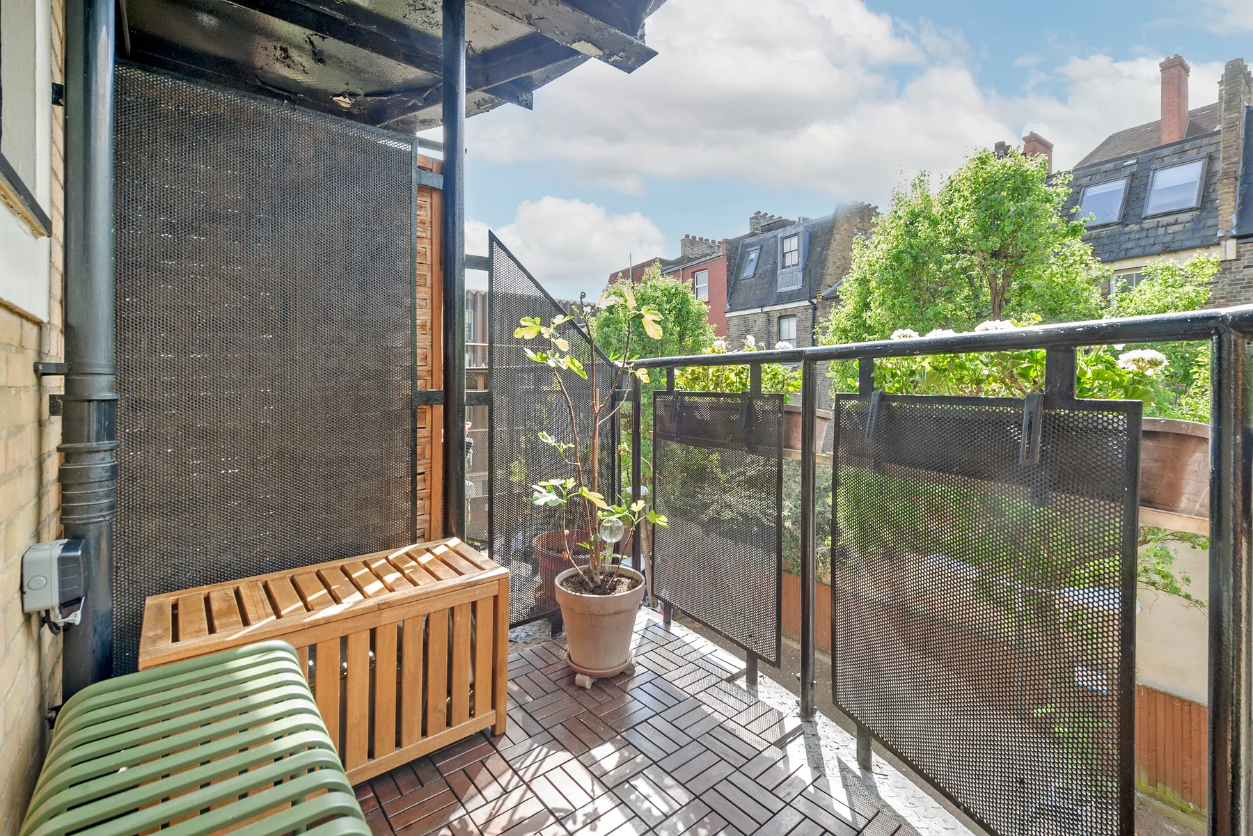 A small outdoor balcony with wooden decking, seating, and potted plants.