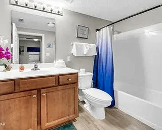 Un baño con un tocador de madera, un inodoro y una cortina de ducha azul.