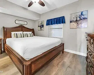 Dormitorio con cama de madera, ropa de cama blanca y una ventana con cortina.