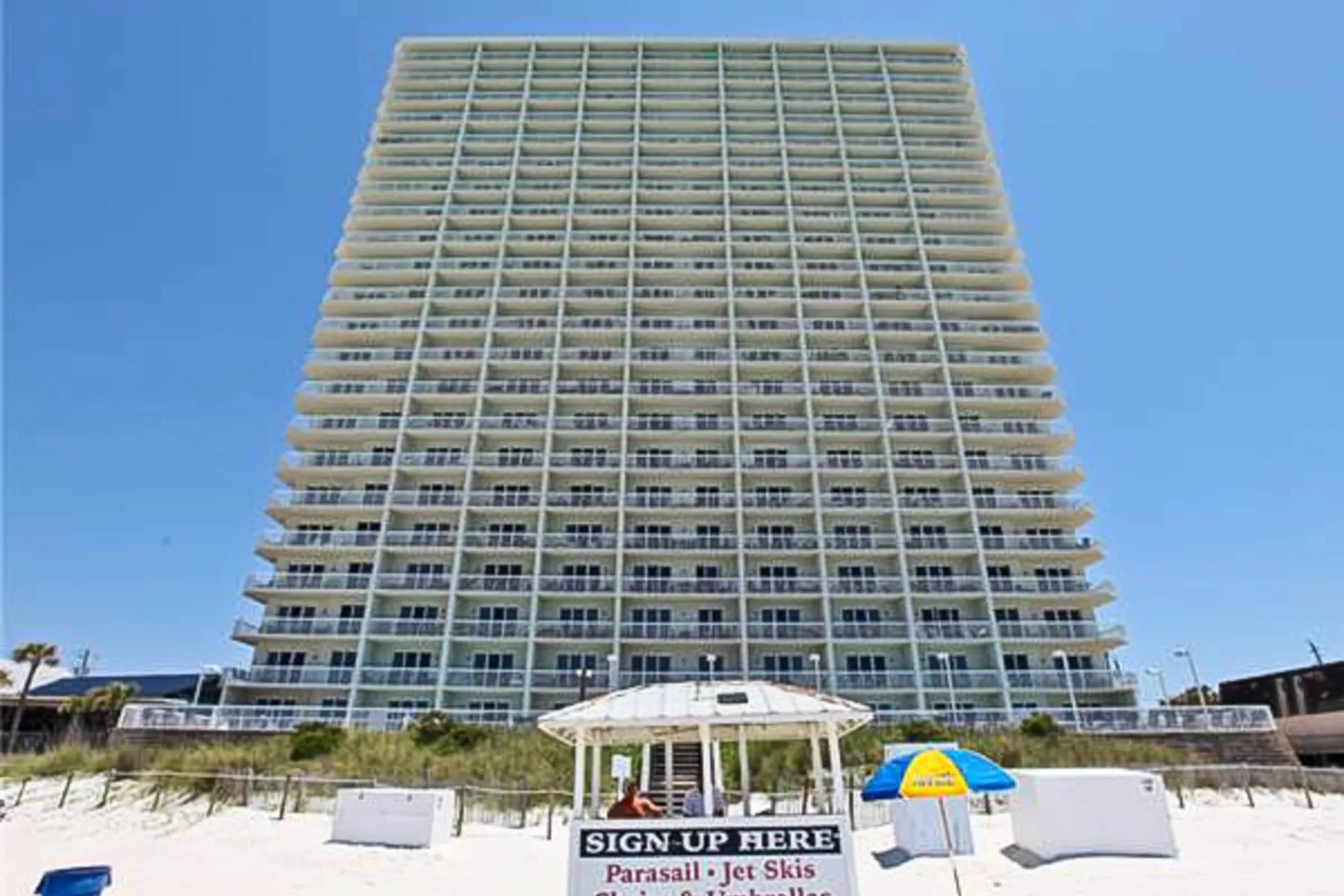 Zona común: Un edificio alto junto a la playa se alza detrás de un pequeño pabellón en la arena.