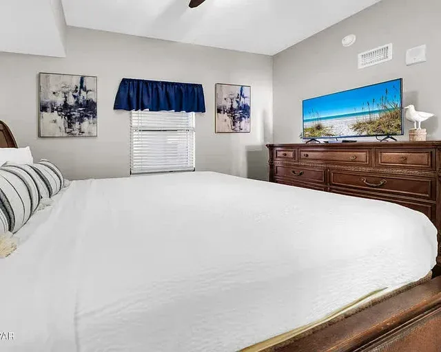 Un dormitorio con una cama grande, una ventana y una cómoda con televisor.