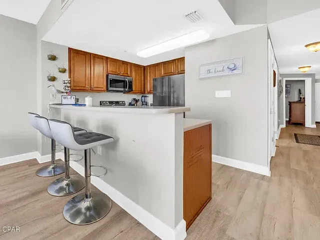 Una cocina con gabinetes de madera, electrodomésticos de acero inoxidable y asientos junto a la barra.